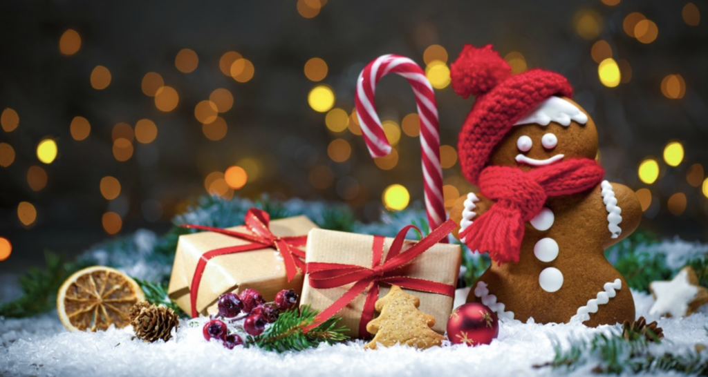 Image of gingerbread man wearing a hat and scarf holding a candy cane surrounded by snow and wrapped presents